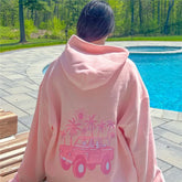 Person wearing a pink hoodie with a graphic design by a pool